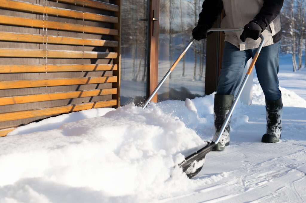 A man in winter clothes with a snow shovel cleaning the snow from the terrace of the house