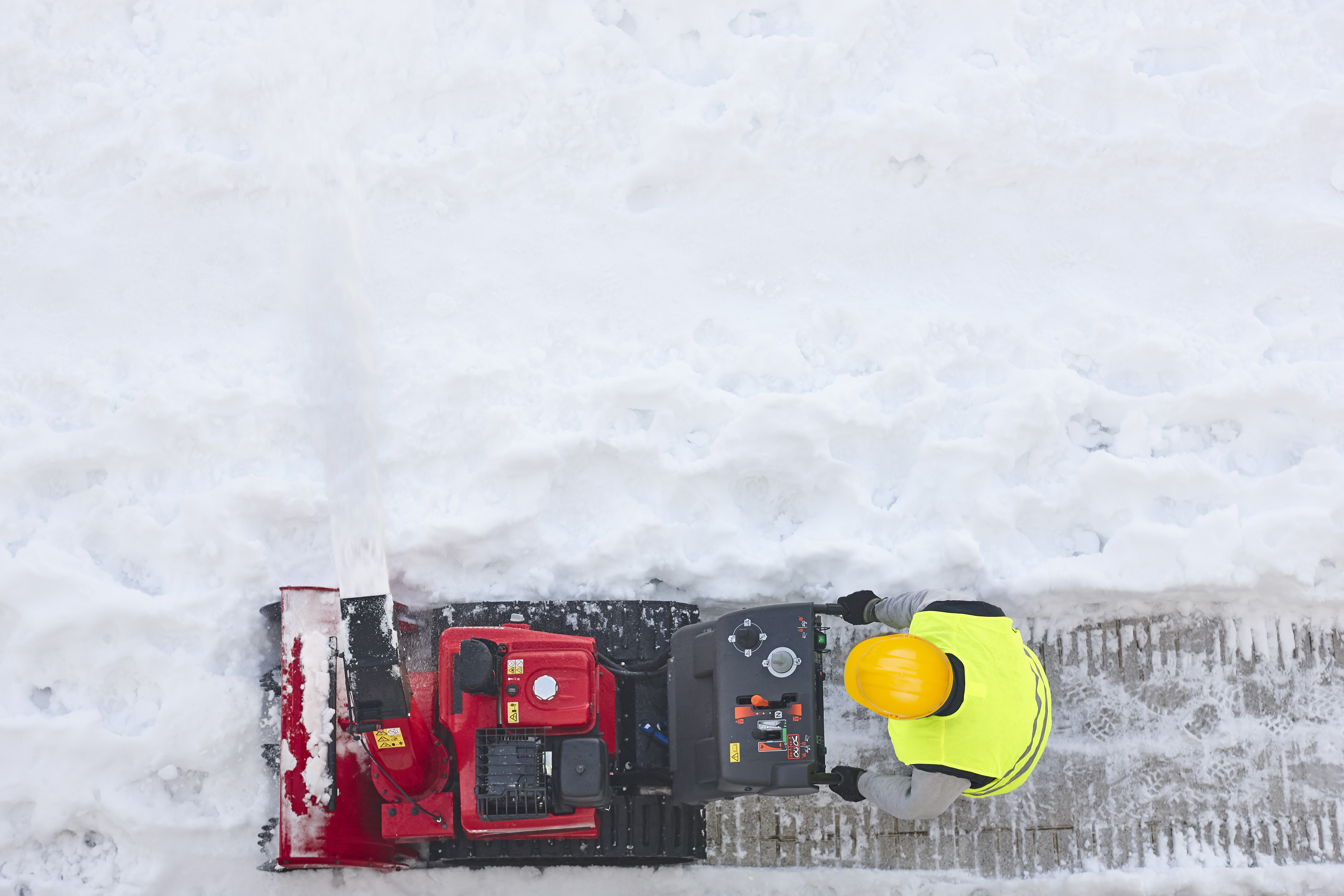 Worker cleaning snow on the sidewalk with a snowblower. Maintenance